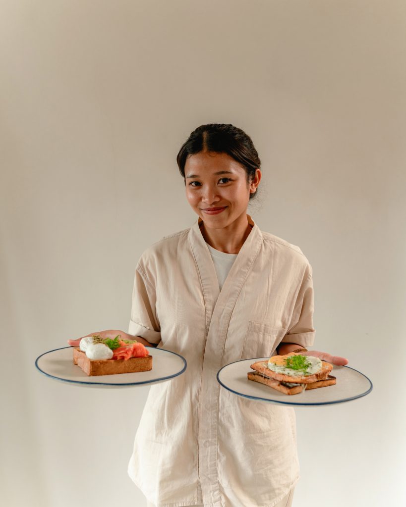 A woman is smiling while carrying two plates of breakfast bread.