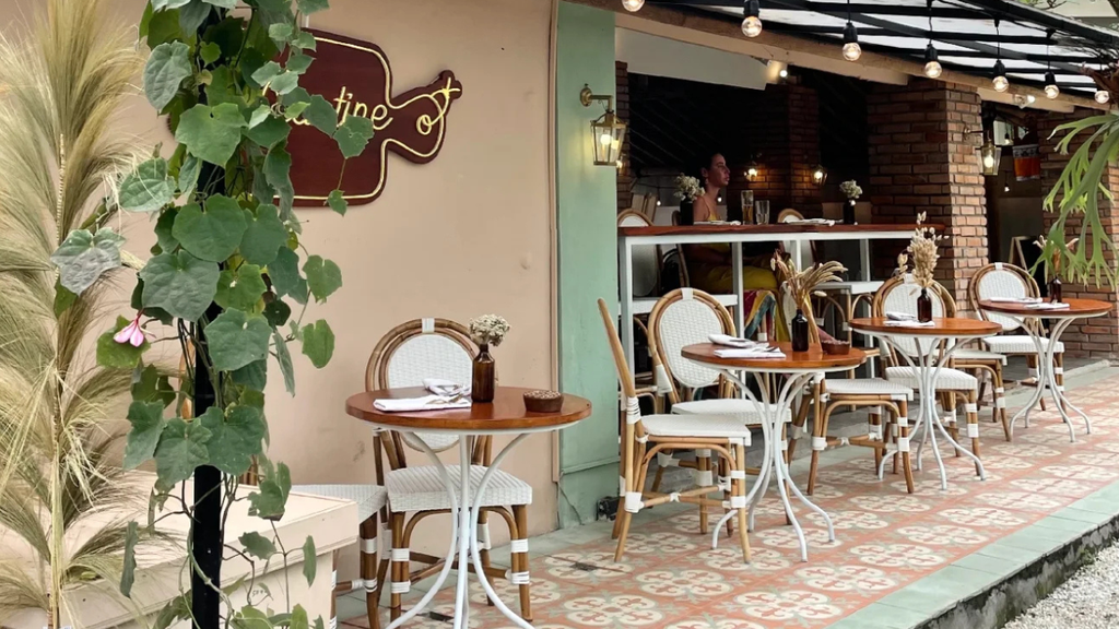 Cozy restaurant terrace with wooden furniture and tropical plants.