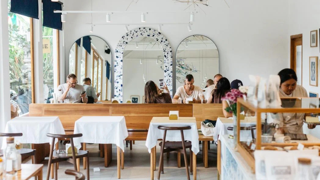 Bright modern café with wooden tables, white chairs, and large windows.